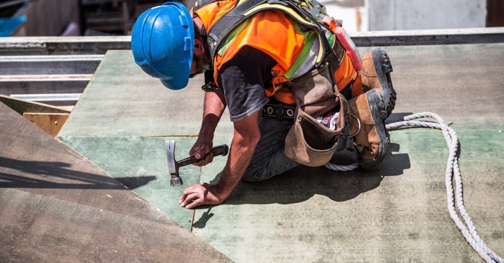 A skilled construction worker in protective gear hammering a rooftop panel.