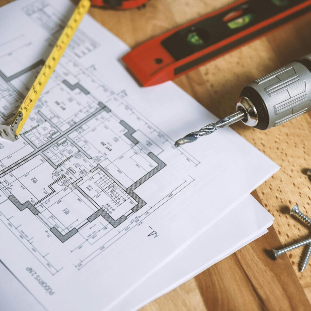 Close-up of construction blueprint with tools like drill and screws on a wooden table.